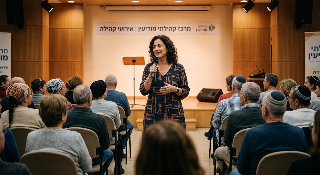 מרצה על במה באולם קהילתי מדברת עם מיקרופון מול קהל מבוגרים